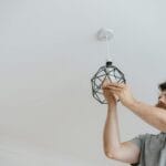 Jak wykonać punkt pod lampę: puszka, hak i podłączenie przewodów bez stresu Elektryk montuje nowoczesną geometryczną lampę sufitową w mieszkaniu
