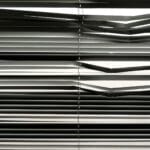 Rolety wewnętrzne a prywatność: jak ograniczyć podgląd bez zaciemniania Poziome żaluzje wewnętrzne tworzące wzór cieni w nasłoneczonym pokoju