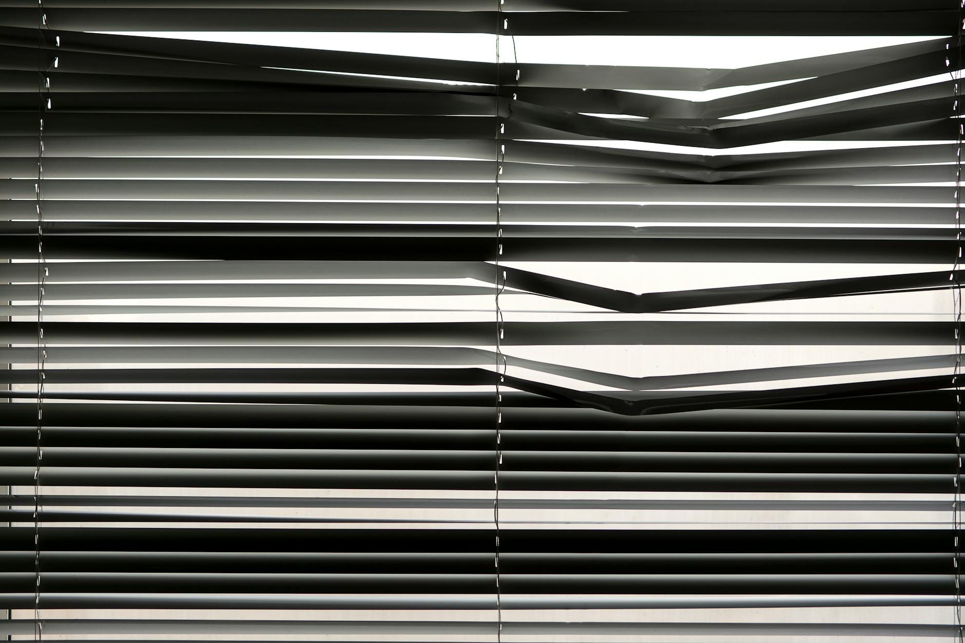 Poziome żaluzje wewnętrzne tworzące wzór cieni w nasłoneczonym pokoju