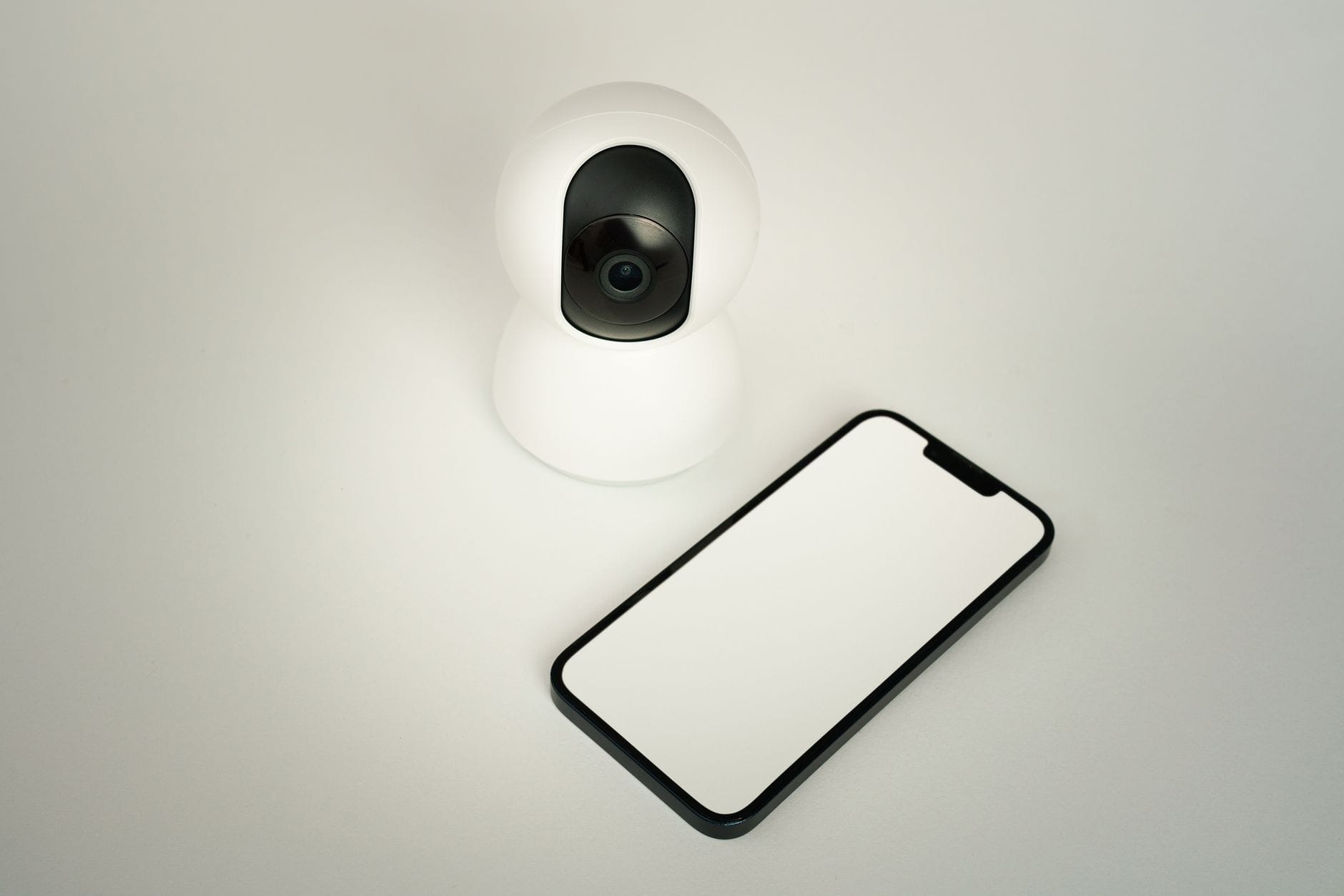 Kamera monitoringu smart home obok smartfona na białym tle