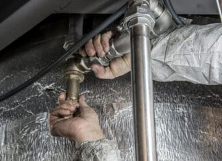 Próba ciśnieniowa instalacji wodnej: jakie ciśnienie zastosować i jak długo testować Zbliżenie dłoni hydraulika montującego stalowe rury wewnątrz budynku